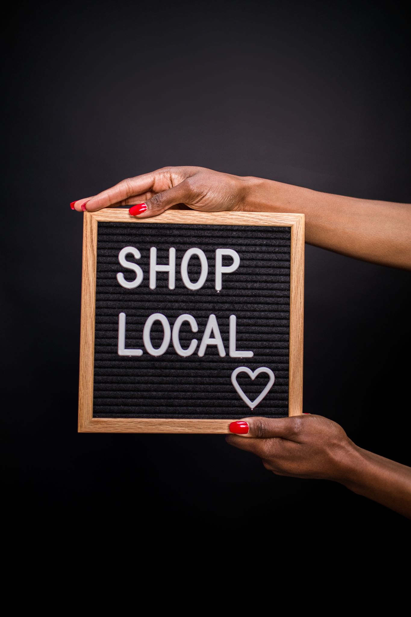 Hands holding a letter board with 'SHOP LOCAL' message on black background, promoting local businesses.